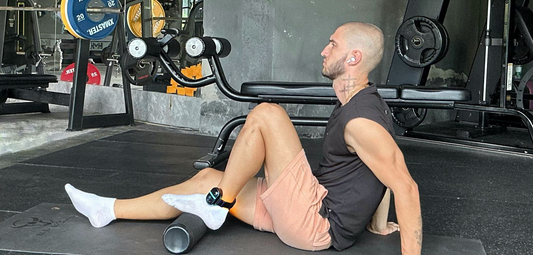 Man using PRUNGO red light therapy while stretching on foam roller in gym