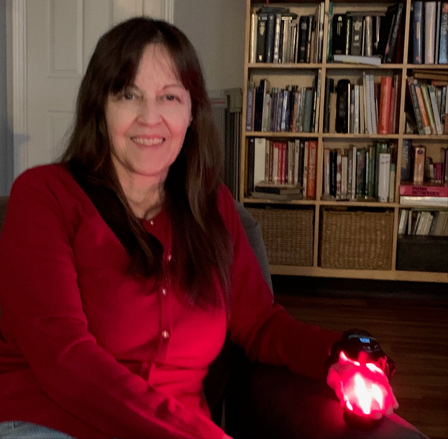 Woman in a red shirt sitting on a couch with prungo red light therapy device